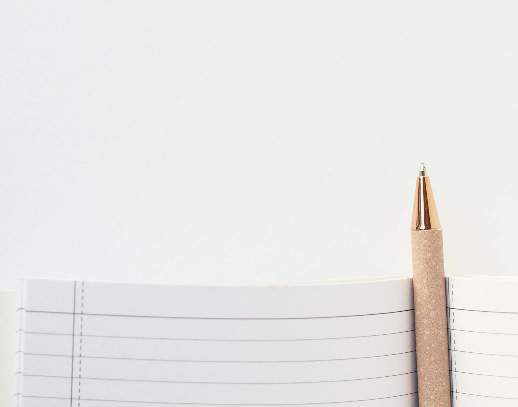 A minimalist photo of a notebook and pen with ample copy space on a white background.